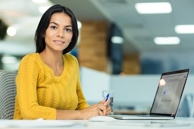 Happy casual businesswoman sitting at the table in office and looking at camera