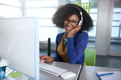 Portrait of a smiling woman with an afro at the computer in bright glass office